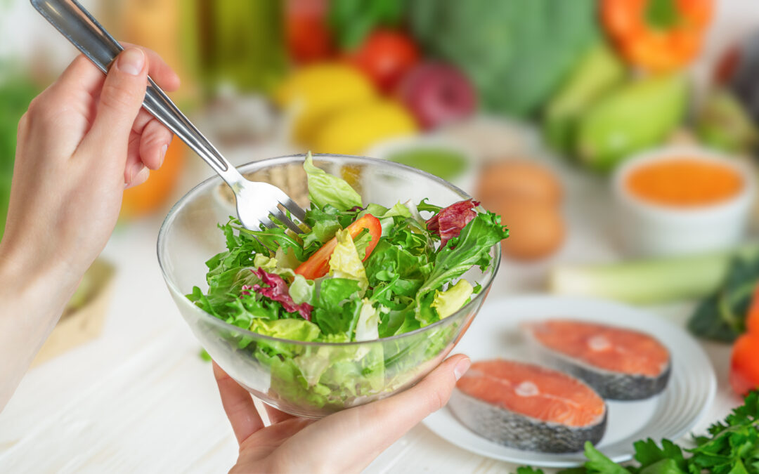 Image of a woman holding a salad bowl with fish and vegetables in the background representing healthy, anti-inflammatory foods